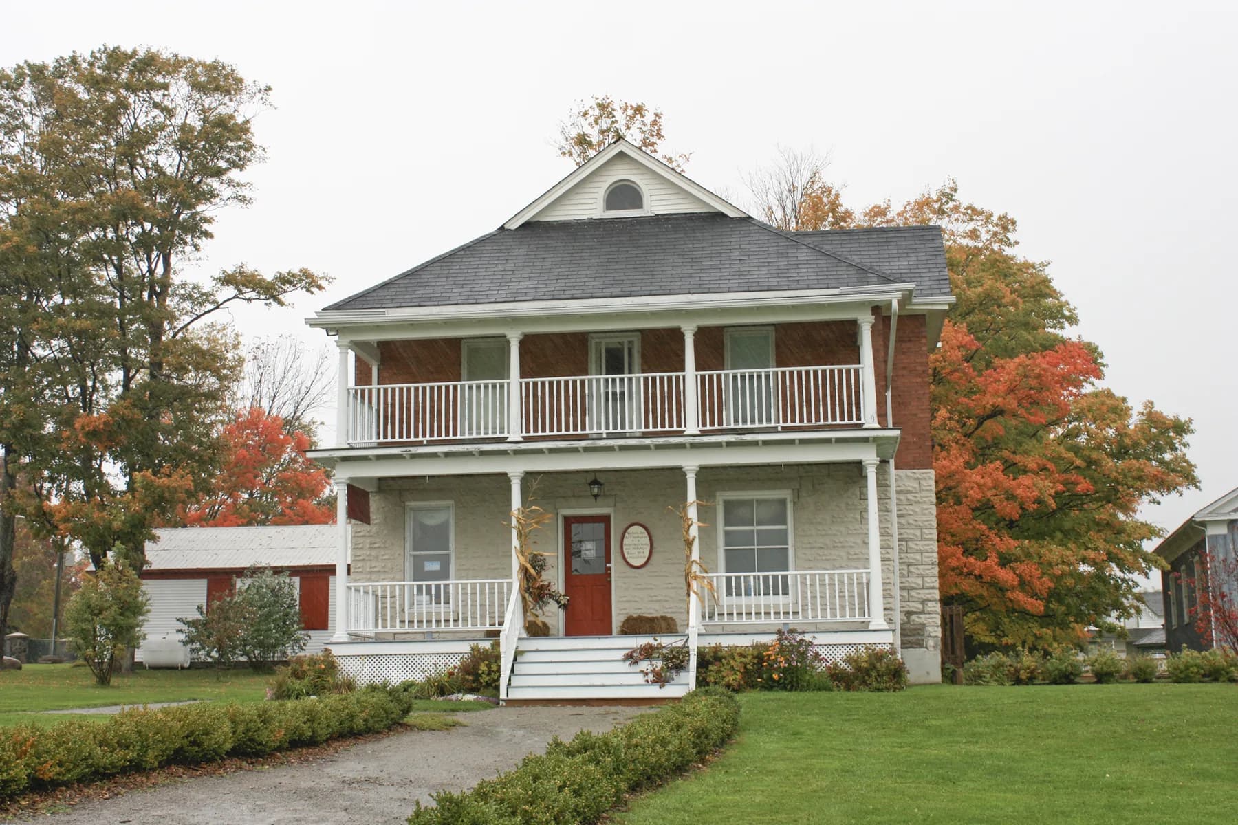 A two-storey heritage house with white porches and autumn trees at Uxbridge Historical Centre.