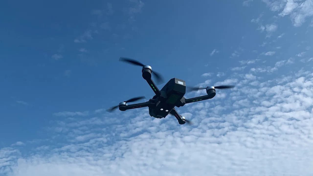 A quadcopter drone in flight against a blue sky; no people visible.