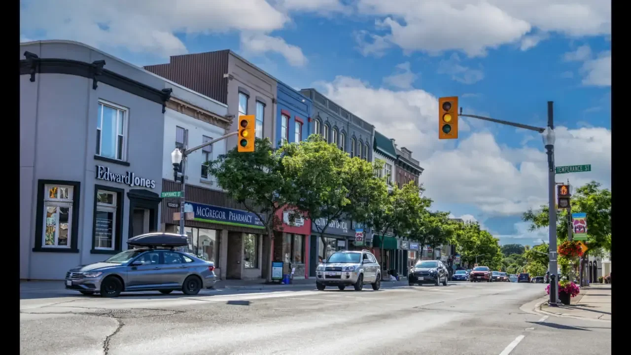 Downtown Bowmanville commercial street with storefronts, traffic lights and parked cars on a sunny day