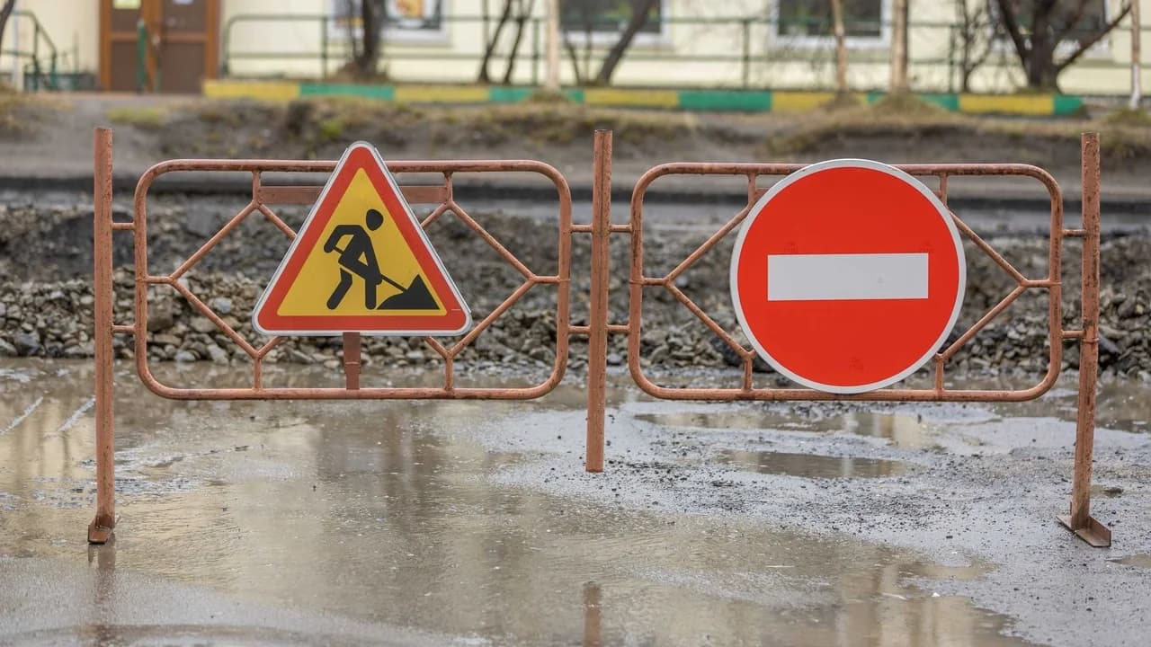 Metal construction barriers with road-work warning signs closing off a work area; no people visible.