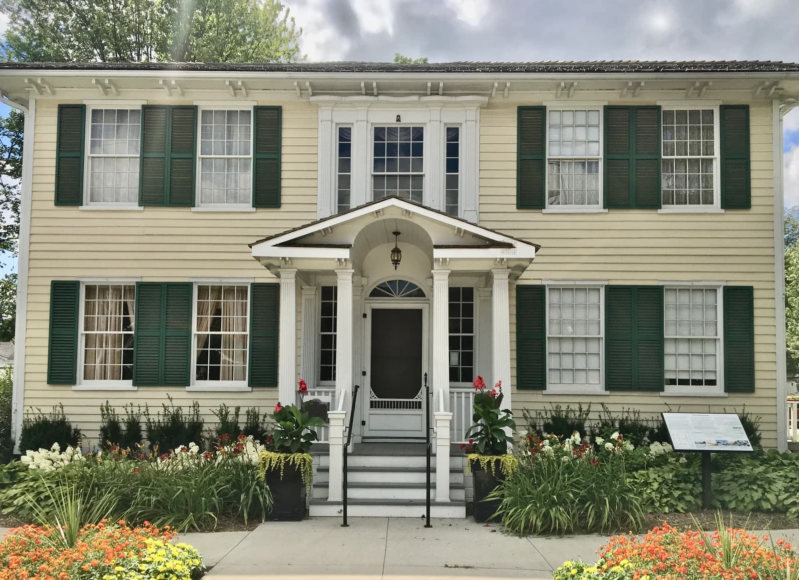 Cream-coloured Lynde House Museum with green shutters, a central porch and flower beds.