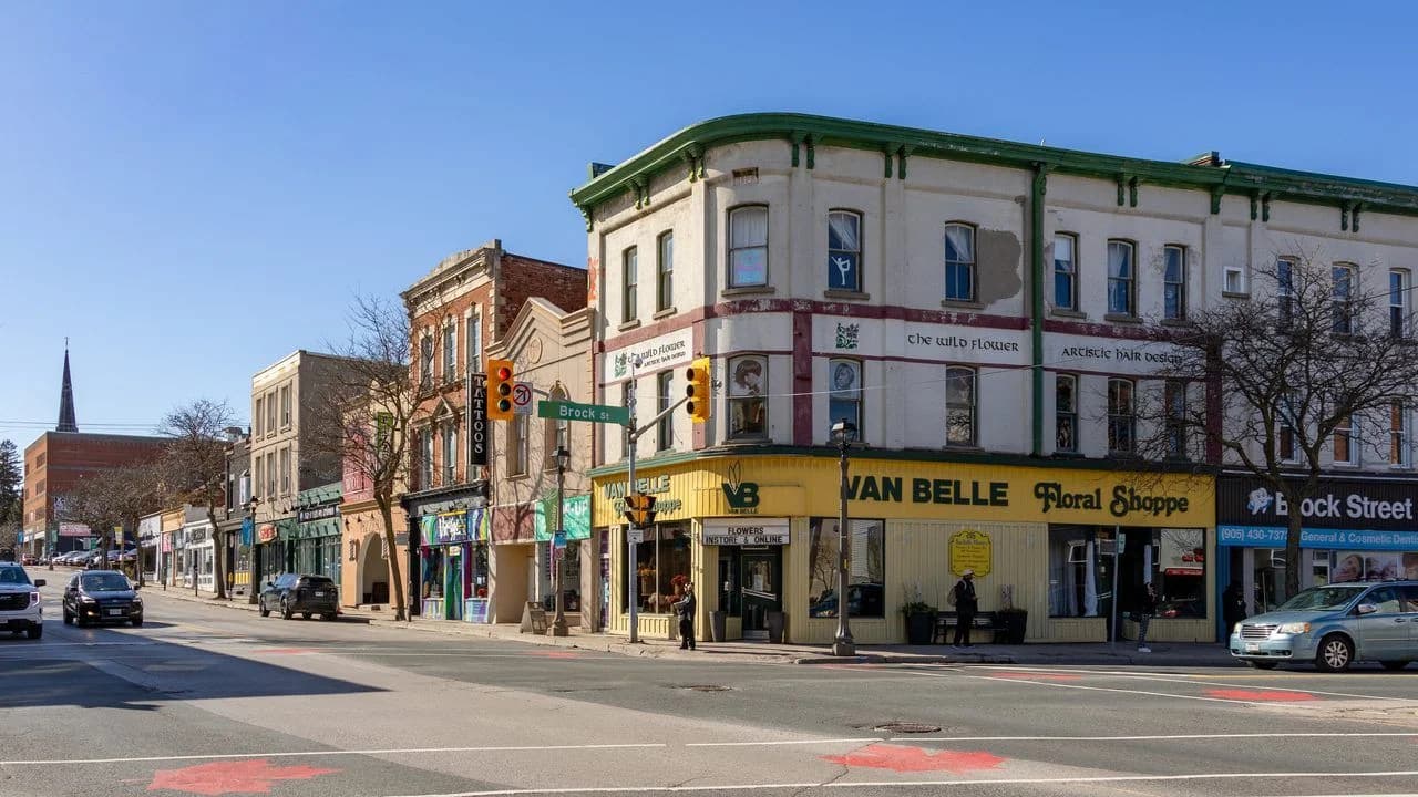 Downtown Whitby streetscape at the corner of Brock Street on a clear day, with heritage storefronts, parked cars and traffic lights; no faces visible