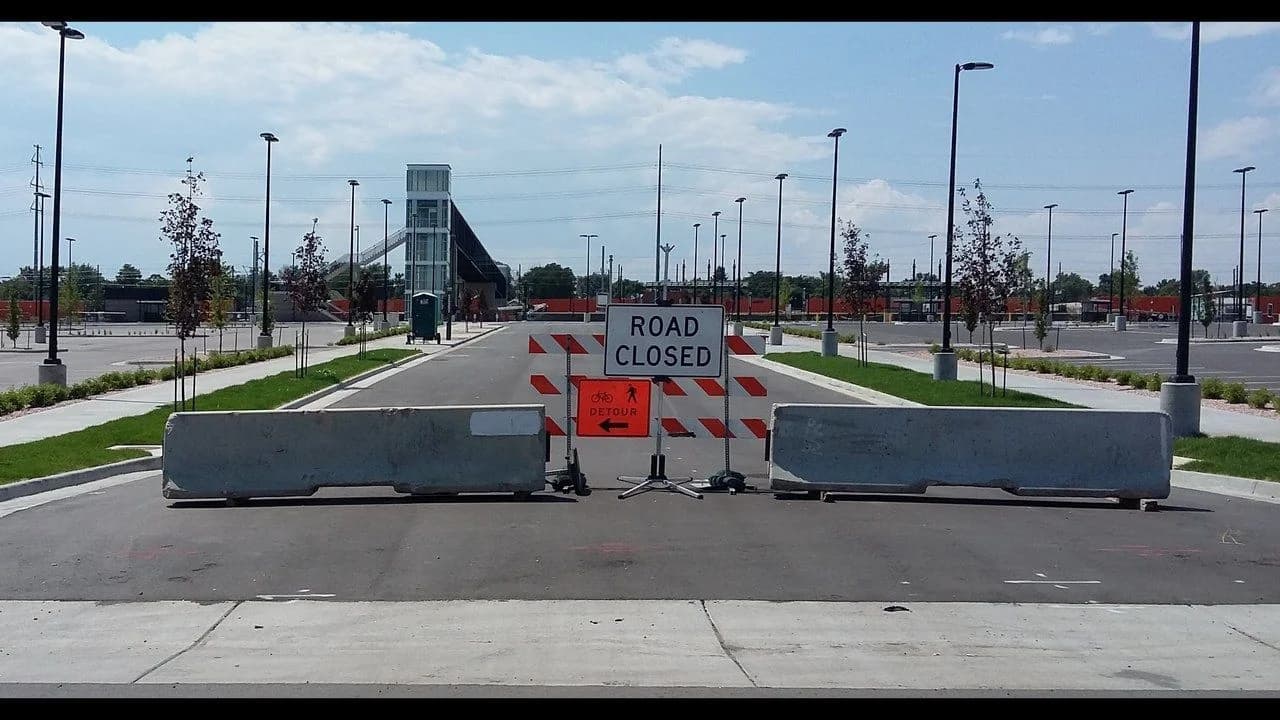 A 'Road Closed' sign with concrete barricades blocking a road; no people present